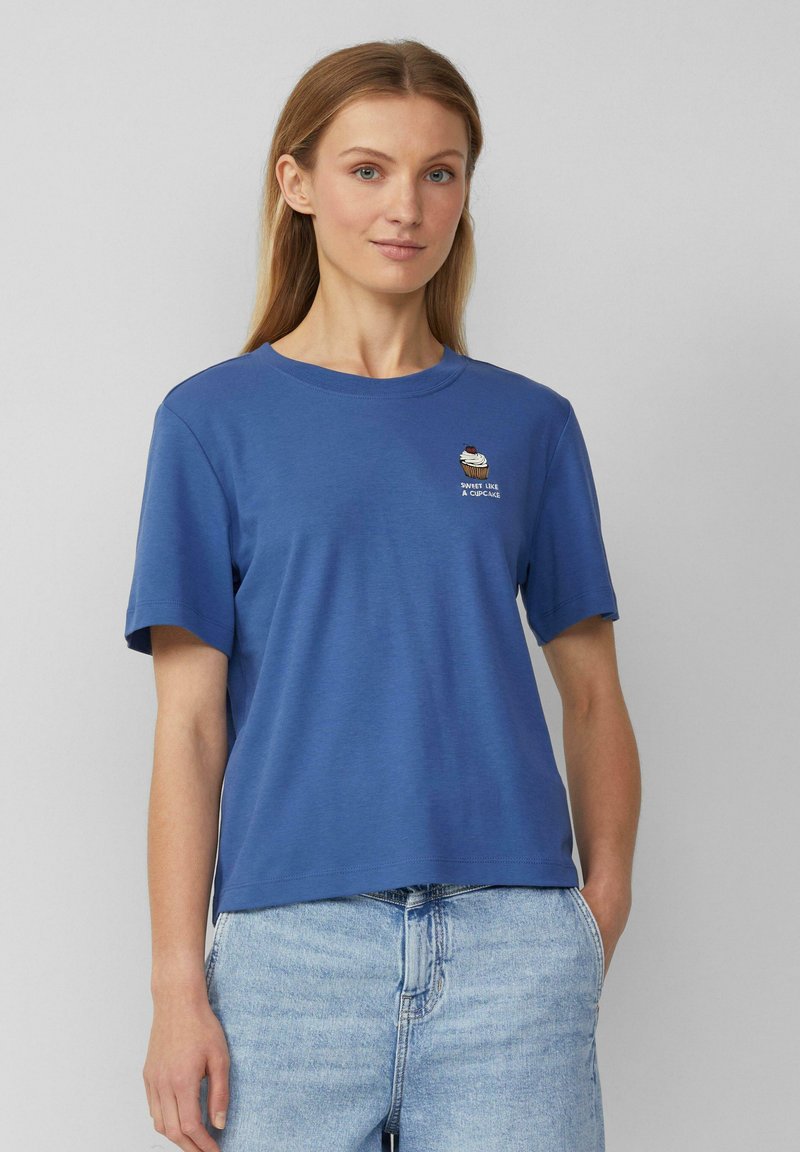 T-shirt bleu à manches courtes en tissu doux. Présente un graphique de cupcake avec le texte "DOUX COMME UN CUPCAKE" imprimé au-dessus.