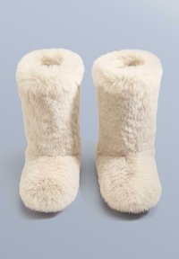 Világos bézs műszőrme csizma, közép-szárú, puha, bolyhos textúrával, lekerekített orral és varrásmentes dizájnnal.