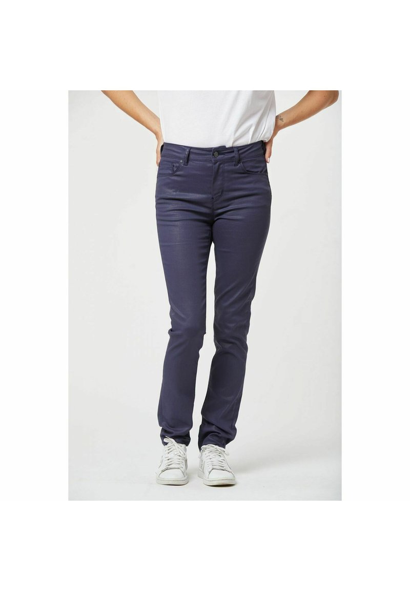Navy blauwe slim-fit jeans gemaakt van een gladde, rekbare stof met voorzakken en een rits, gecombineerd met witte sneakers.