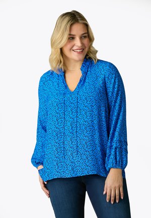 Blouse à motifs bleus avec un décolleté en V, des manches longues et des poignets froncés. Fabriquée dans un tissu léger avec un dessin à peine specklé.