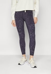 Violet leggingai su gepardų raštu, pasižymintys prigludusia forma ir tekstūruotu audiniu. Kartu derinami su šviesių atspalvių sportiniais batais.