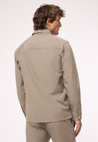 Beige Jacke aus glattem Stoff, mit klassischem Kragen, langen Ärmeln und knappengefertigten Manschetten. Schlichtes Design ohne auffällige Muster.