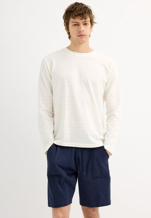 Top de manga larga color crema, hecho de una tela ligera, combinado con pantalones cortos azul marino que cuentan con dos bolsillos frontales y una cinturilla elástica.