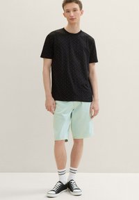 Black short-sleeve shirt with small colorful dots, paired with light mint-green shorts. Black sneakers with white soles and striped socks.