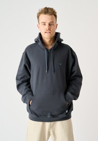 Dunkelgrauer Pullover-Hoodie aus weichem Stoff, mit einer Fronttasche, verstellbaren Kordeln und einem kleinen tealfarbenen Logo auf der Brust.