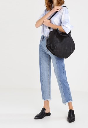 Woman wearing cropped two-tone jeans, light blue plaid shirt, black slip-on shoes, and carrying a large black leather shoulder bag.