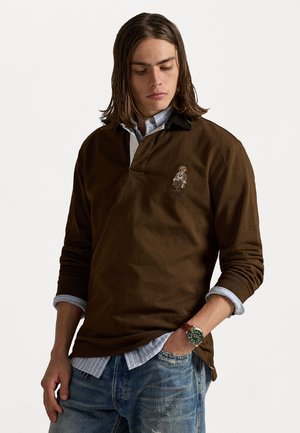 Brown long-sleeve polo shirt with a contrasting collar, featuring an embroidered figure and paired with a light blue checkered shirt underneath.