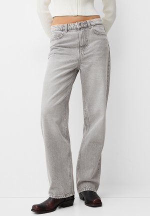 Vrouw draagt lichtgrijze rechte jeans met hoge taille, zwarte leren enkellaarzen en een wit cropped geribd truitje.