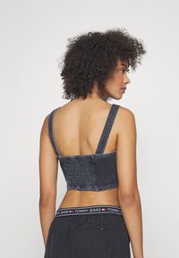 Farmer dzseki crop top széles pántokkal, sötét mosással és ráncolt hátrésszel. Fekete nadrággal kombinálva, amely logós derékrésszel rendelkezik.