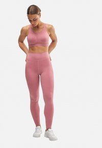 Sujeción deportiva rosa y pantalones leggings de cintura alta a juego, hechos de un tejido elástico. Presenta un diseño ajustado, estilo minimalista y una marca sutil.