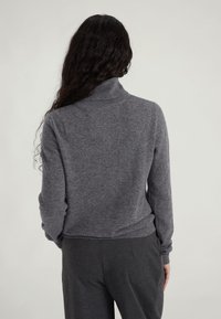 Un pull gris à col montant, avec un col côtelé et de longues manches, offrant une texture douce et un design court. Associé à un pantalon gris foncé.