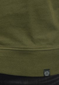 Olivengrüner Sweatshirt mit geripptem Saum und strukturiertem Stoff. Bietet ein kleines schwarz-weißes Markenlabel.