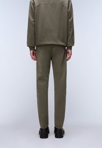 Olivgrön sweatshirt och matchande byxor, med en slät yta och avslappnad passform. Bärs med svarta skor, sedd bakifrån.