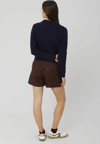 Pull en tricot bleu marine, longueur raccourcie, associé à un short écossais bordeaux avec un ourlet festonné ; baskets blanches avec des accents noirs.