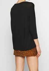 Czarna, długorękawowa bluzka o luźnym kroju z zaokrąglonym dekoltem w połączeniu z krótką, prążkowaną spódnicą w brązowo-czarny wzór w cętki lamparta.