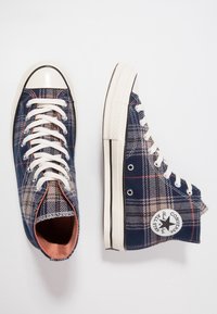Hochhalsige Sneaker in Marineblau mit karriertem Muster. Hergestellt aus Canvas mit weißen Gummispitzen und Schnürsenkeln. Verfügt über ein Logopatch an der Seite.
