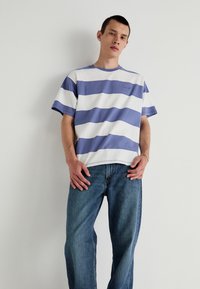Camiseta riscada em algodão lavanda e branca, com riscas horizontais e decote redondo, combinada com jeans de denim azul claro.