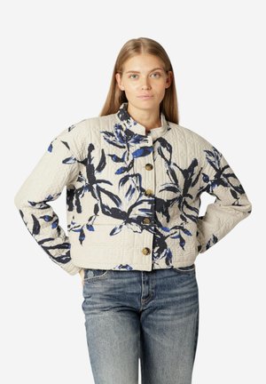 Chaqueta bomber acolchada en marfil con un patrón floral azul y negro, con un alto cuello y botones dorados, combinada con jeans azules.