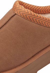 Brun suede tøfler med en struktureret, hørmønsteret orange kant omkring kraven og en glat sål.