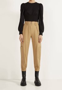 Zwart cropped topje met pofmouwen gecombineerd met beige cargobroek met zijzakken en een kettingaccent, gedragen met zwarte plateau laarzen.