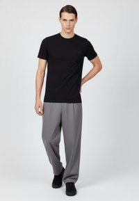 Svart t-shirt med kort ärm och rund halsringning, tillsammans med löst sittande grå byxor och svarta sneakers på en enfärgad bakgrund.