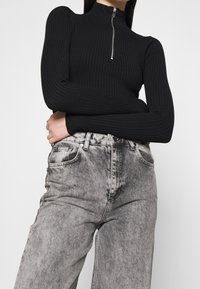 Svart ribbad polotröja med dragkedjedetalj, kombinerad med blekta grå högmidjade jeans med ljus tvätt och framfickor.