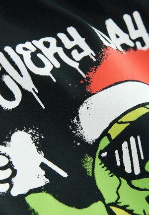 Juodas tekstilės audinys su dizainu, kuriame žalias veikėjas dėvi akinius nuo saulės ir raudoną skrybėlę. Tekstas „LABAI“ ir „DIENA“ baltu grafiti stiliumi.