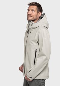 Hellgraue wasserdichte Jacke mit Kapuze, ausgestattet mit einem Frontreißverschluss und Reißverschlusstaschen an den Seiten. Glatte Textur mit verstellbaren Bündchen.