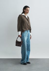 Brązowa koszula w kratę zapinana na guziki z białym kołnierzykiem, niebieskie jeansy o szerokich nogawkach z srebrnymi ozdobami w kropki oraz bordowa torba. Czarne buty.