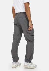 Szare spodnie cargo z elastycznym pasem i licznymi kieszeniami, z zamkami błyskawicznymi i zwężanymi mankietami, w komplecie z białymi trampkami.