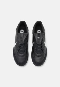 Zapatillas negras con parte superior de cuero y ante, con un swoosh blanco en contraste, cordones redondos y acolchado en el collar. Suela de goma plana para agarre.