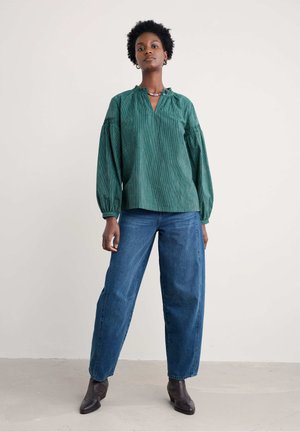 Groen gestreepte blouse met een hoge halslijn en pof mouwen, gecombineerd met losse blauwe spijkerbroeken en zwarte enkellaarsjes.