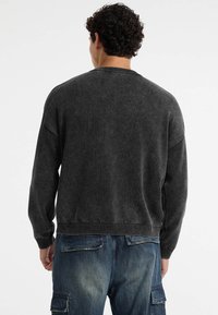 Donkergrijze sweater met een gestructureerde afwerking, geribbelde hals en tailleband, en drop shoulders, gecombineerd met blauwe cargobroek.