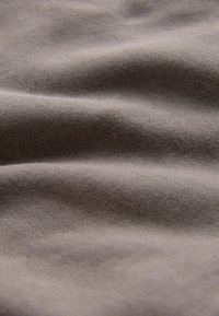 Gaiši brūns audums ar gludu, teksturētu virsmu, kas satur salocītas, nedaudz krunkotas sekcijas un vienkāršu auduma rakstu.