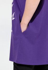 Lila bomull t-shirt med sidfodral. Har en avslappnad passform och en slät textur. Sömmen är rak och något längre bak.