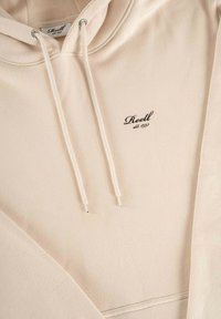 Beige Kapuzenpullover aus weichem Stoff, mit einer Kordel mit metallenen Enden und einem in Schwarz gestickten Logo. Einfaches, minimalistisches Design.
