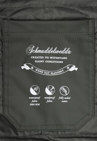 Melnas ūdensnecaurlaidīgas auduma kabatas ar baltu tekstu. Iekļauti ikonas, kas norāda uz ūdens necaurlaidību, vēja necaurlaidību un pilnībā aizzīmogotām šuvēm. Zīmola birka: Schmuddelwedda.