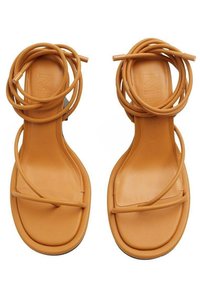 Sandales en cuir marron avec plusieurs sangles torsadées, design ouvert à l'avant, semelle plate et surface lisse. Style minimaliste sans accents en matériel.