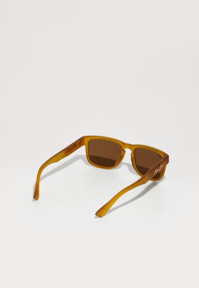 Bruntone solbriller med en gennemsigtig amber stel, firkantede glas og slanke stænger med et logo på siden.