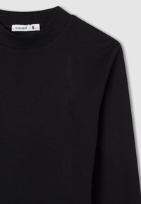 Czarny prążkowany top z długim rękawem i okrągłym dekoltem. Materiał wydaje się miękki i ma teksturowaną powierzchnię. Widoczna metka z informacjami o marce i rozmiarze.