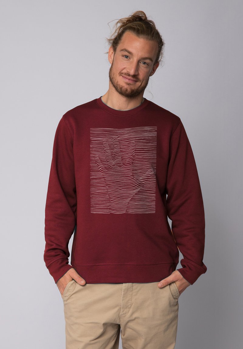 Sweat à col rond bordeaux avec un graphique texturé en blanc représentant une main au milieu de lignes ondulées, avec des poignets côtelés.