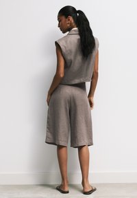 Svetlohnedý ľanový outfit pozostávajúci z bezrukávového crop topu a šortiek po kolená. Dizajn má voľný strih a hladkú textúru.