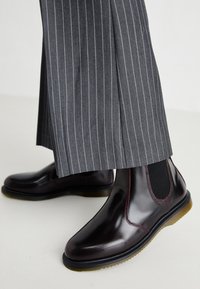 Burgunderfargede lær ankle boots med elastiske sidepaneler og en teksturert såle, kombinert med grå stripete bukser.