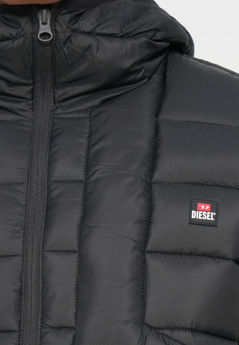 Zwarte gewatteerde pufferjack met rits aan de voorkant en Diesel-logo patch op de borst.