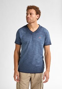 Námořnická modrá v-krční tričko s texturovaným gradientem, krátkými rukávy a malým červeným logem na levé hrudi. Vyrobeno z lehkého materiálu.