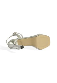 Zilveren sandalen met hoge hakken, voorzien van glinsterende banden en een verstelbare enkelgesp. Heeft een gladde, lichtgekleurde zool en een vierkante hak.