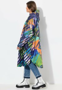 Cappotto impermeabile a colori vivaci con cappuccio, caratterizzato da un motivo geometrico nei toni del blu, verde, arancione e viola, realizzato in materiale leggero.