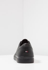 Černé kožené sneakers s texturovaným svrškem, zaobleným podpatkem a gumovou podrážkou. Obsahují malé barevné logo na zadní straně.
