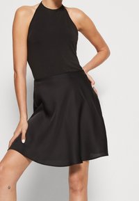 Svart ärmlös halterklänning i mjuk tyg, med en flödande kjol och en något utställd nederkant samt en figurnära bodice.