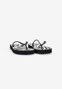 Chanclas negras con una plantilla blanca estampada que presenta líneas abstractas en negro. Suela gruesa negra y correas de plástico.